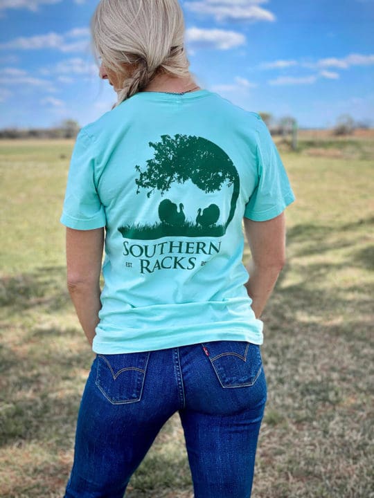 the back of a mint green t-shirt with a dark green screen printed circular silhouette of tree branches and two long beard gobblers with Southern Racks printed underneath the image